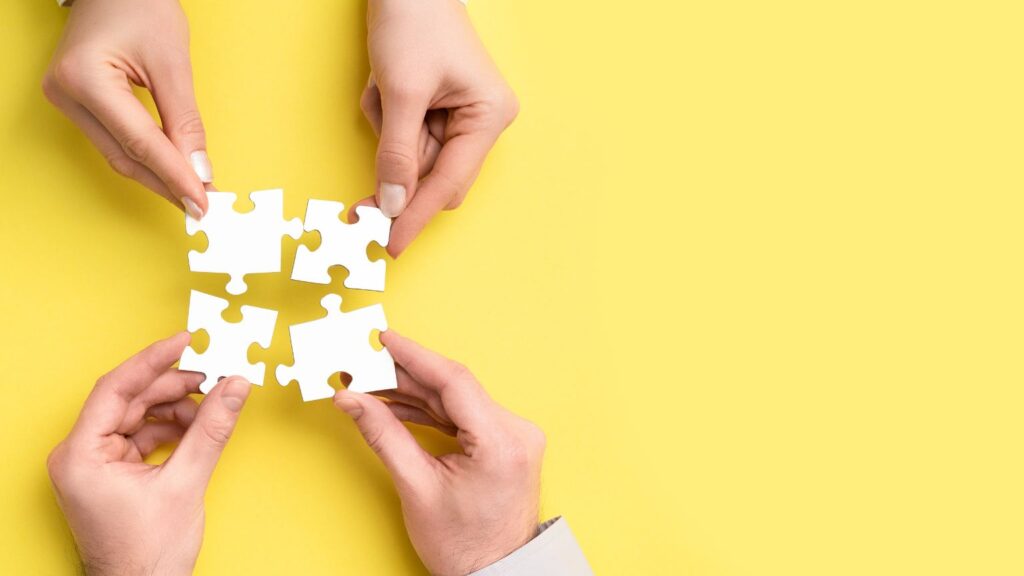 4 mani uniscono un puzzle su sfondo giallo