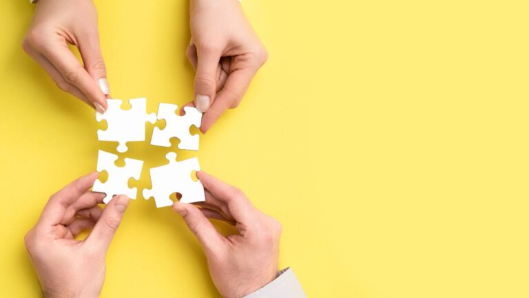 4 mani uniscono un puzzle su sfondo giallo