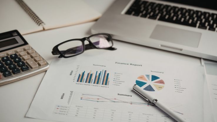 scrivania con indicatori finanziari, computer e occhiali