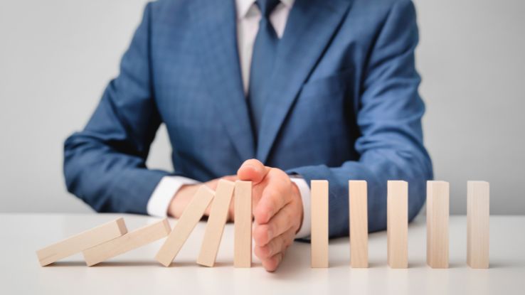 uomo blocca con la mano dei blocchetti di legno che stanno cadendo a simbolo del prevenire la crisi di impresa con strumenti di previsione finanziaria